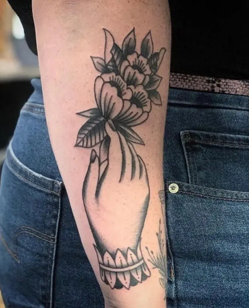 a tattoo of a hand holding flowers on the arm