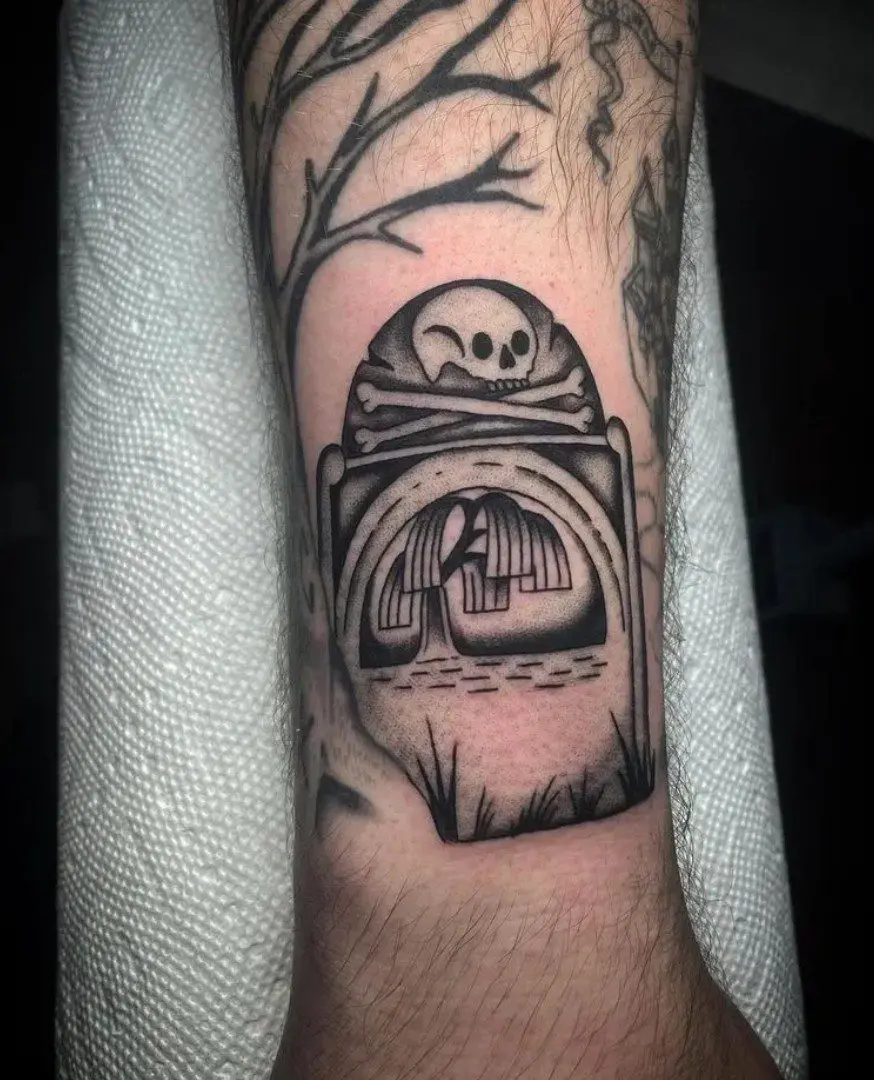 A black and white tattoo of a skull in a grave yard.