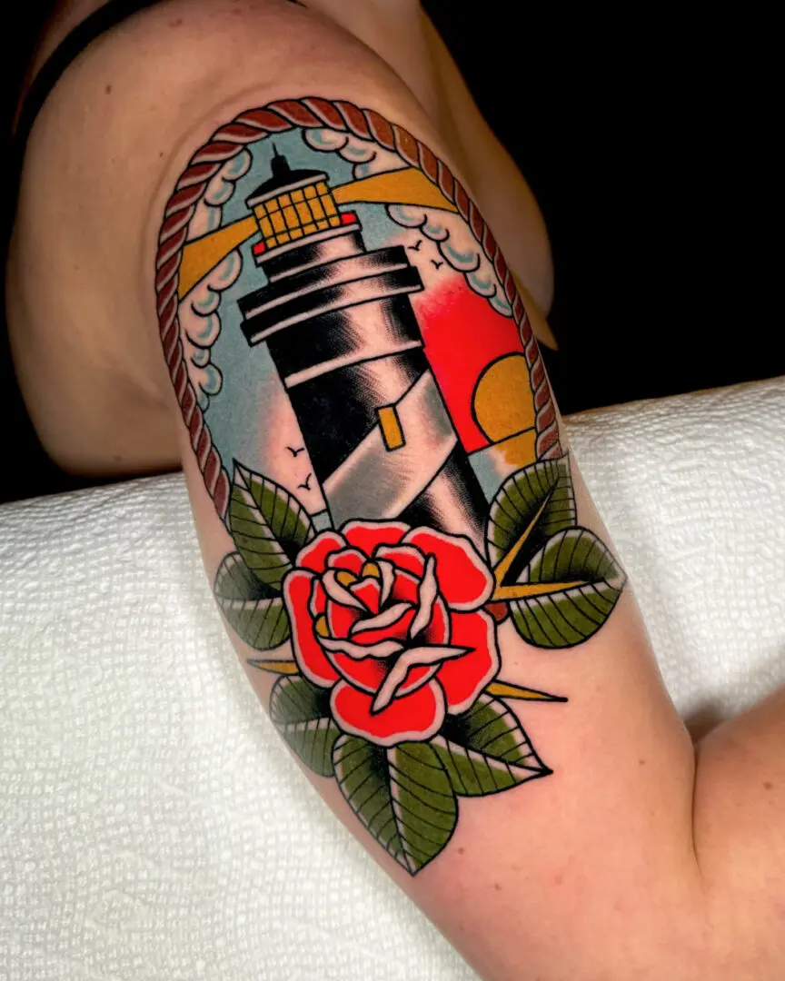 A tattoo of a lighthouse and rose on the arm. Best American Traditional Tattoo Artist- Myke Chambers