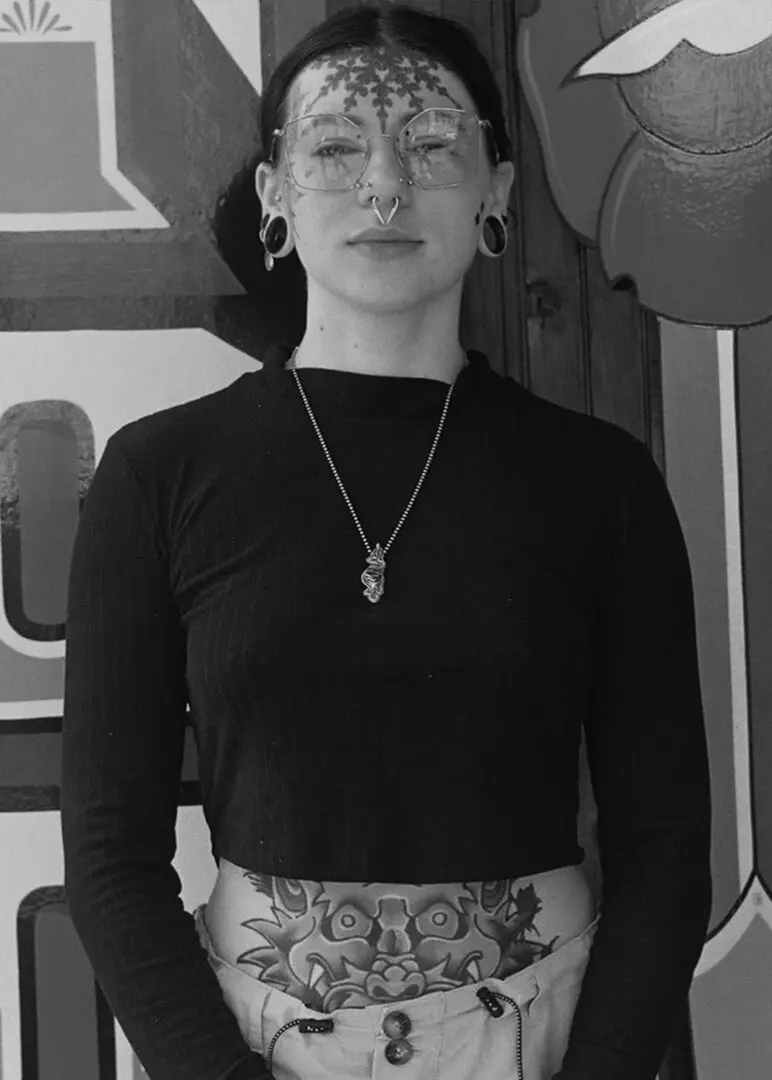 A woman wearing glasses and a hat standing in front of a wall.