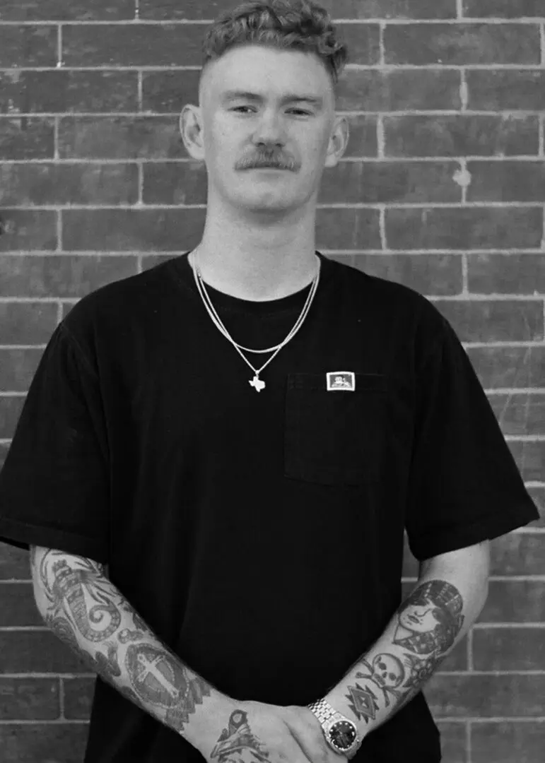 A man with tattoos standing in front of a brick wall.