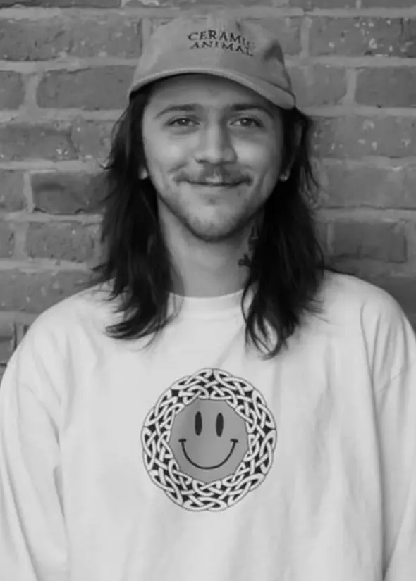 A man with long hair and a hat is smiling.