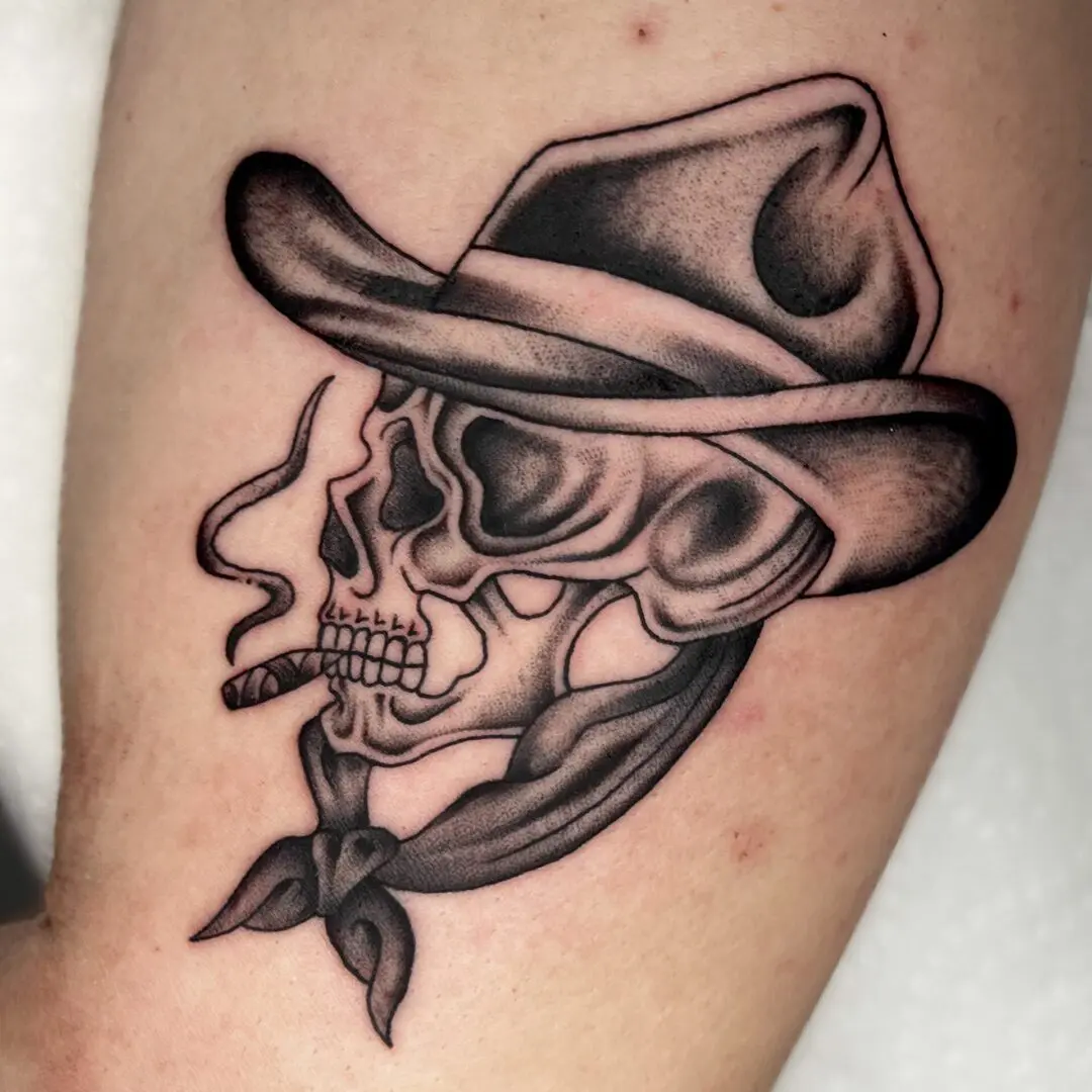 A traditional black and gray tattoo of a skull wearing a cowboy hat and smoking a cigarette.