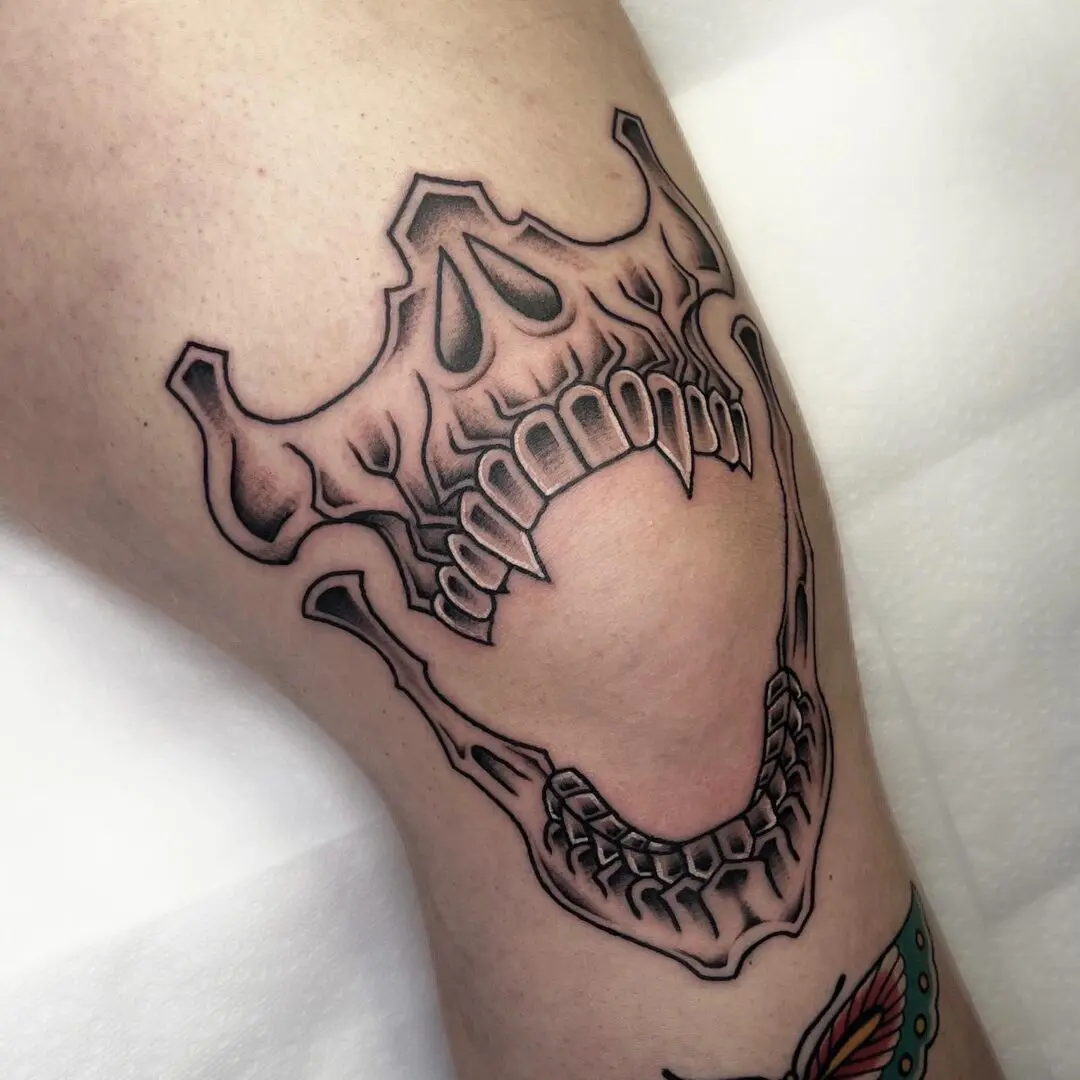 A black and gray traditional tattoo of a skull with teeth on it.