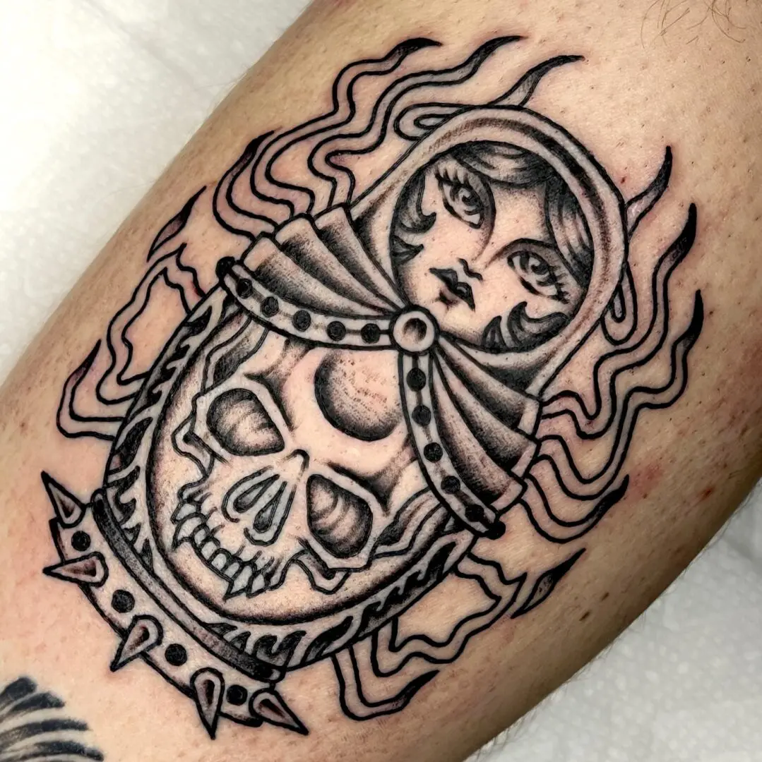A traditional black and gray tattoo of a woman with a skull and flames on her thigh.