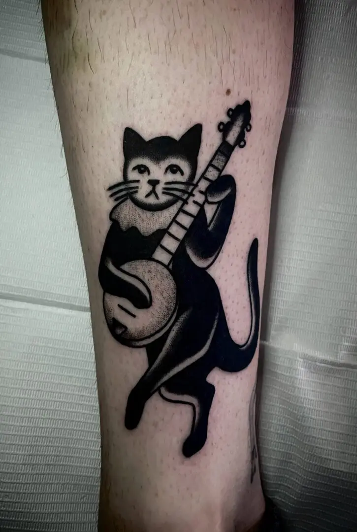 A black and white tattoo of a cat playing a banjo, designed by an Asheville Tattoo Artist.