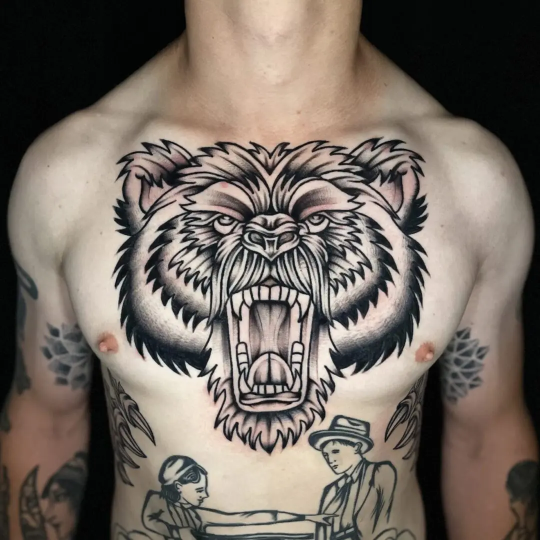 A man with a black and gray traditional bear tattoo on his chest.