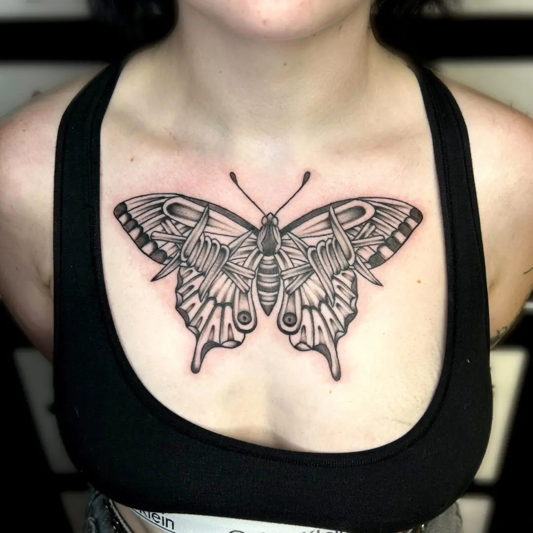 A woman with a black and gray traditional butterfly tattoo on her chest.
