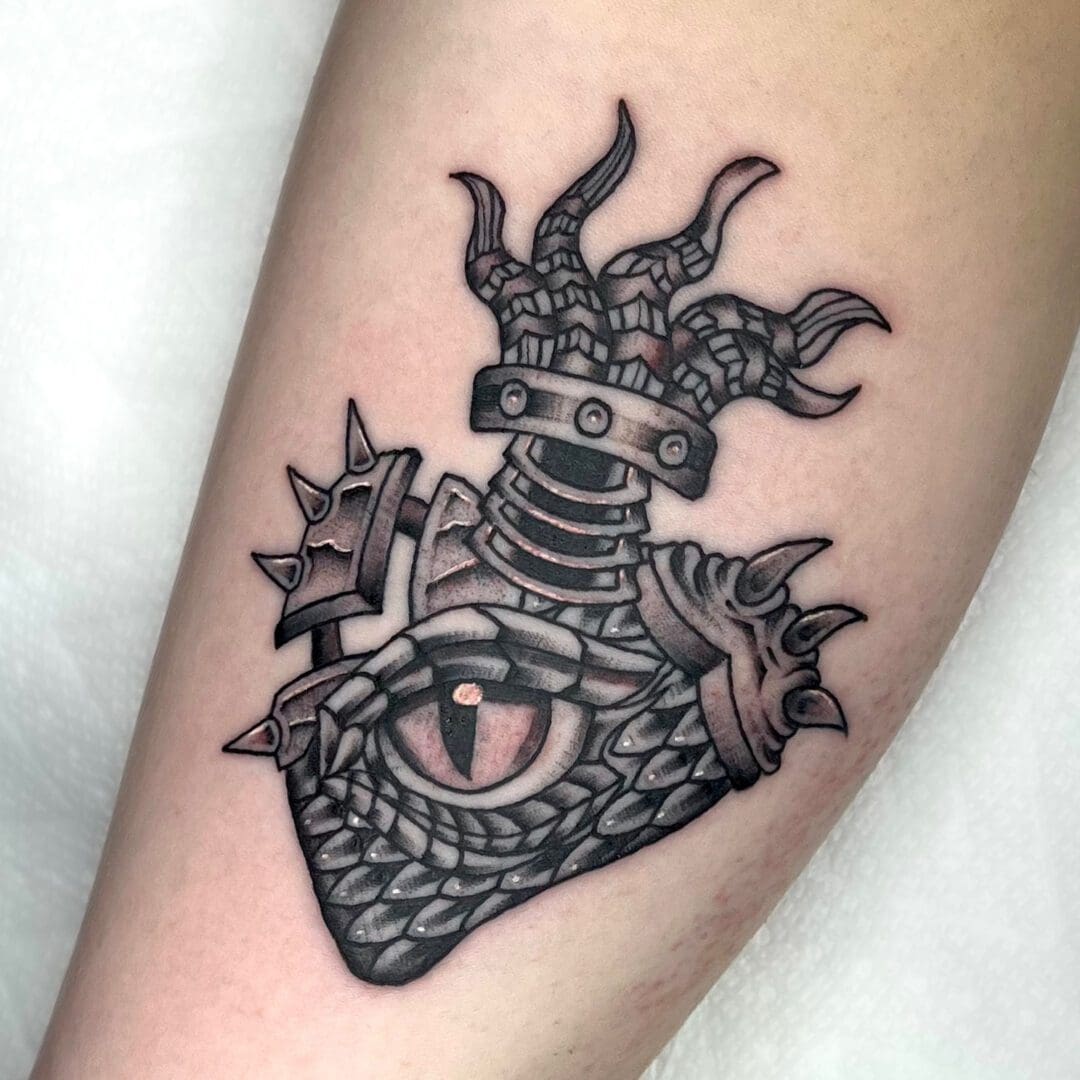A tattoo of a heart with a dragon on it in black and gray traditional style.