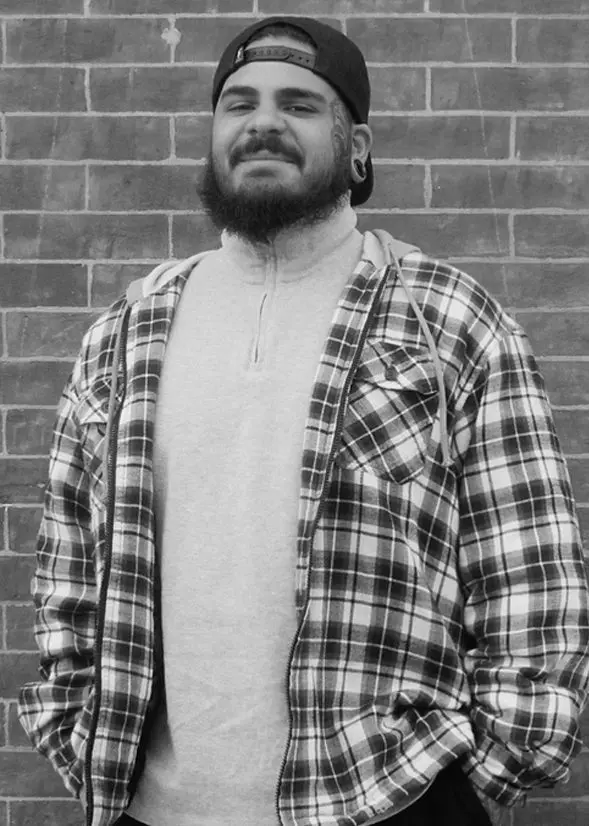 A black and white photo of a man in a plaid jacket, known as one of the Asheville tattoo artists.