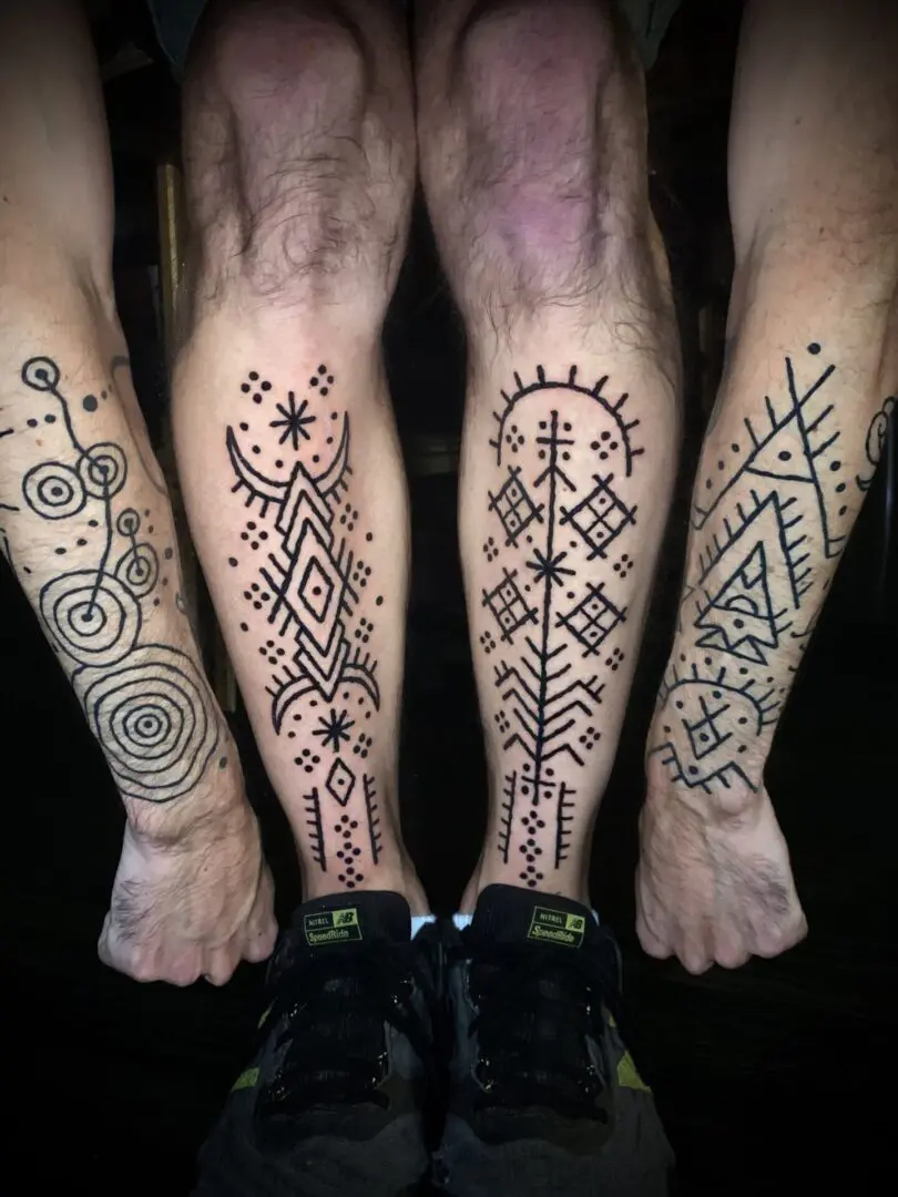 Two men with tribal blackwork tattoos on their legs.
