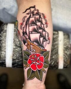 Sailing ship and rose tattoo on arm.