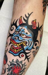Colorful demon mask tattoo on human leg.