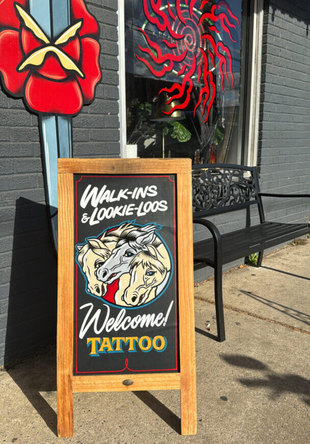 A sign that says " welcome tattoo " on the sidewalk.